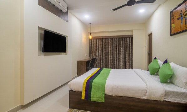 A hotel room with a bed, a desk, a flat-screen TV, a ceiling fan, and a painting on the wall.
