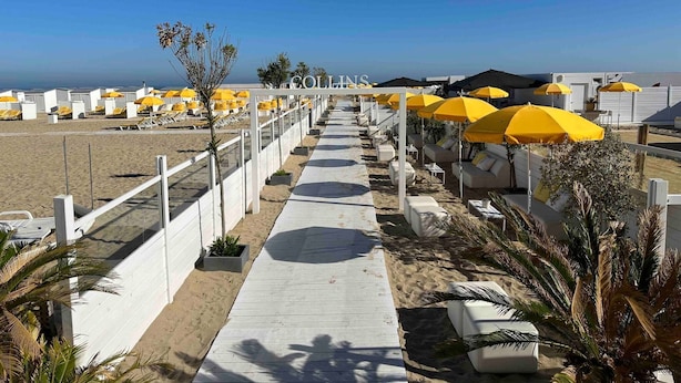 A beachside hotel with a walkway lined with yellow umbrellas and white lounge chairs.