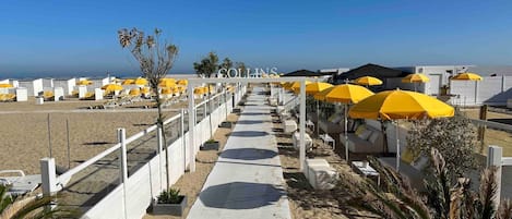A beachside hotel with a walkway lined with yellow umbrellas and white lounge chairs.