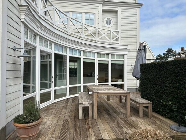 A curved exterior with large windows, a wooden deck, and a potted plant.