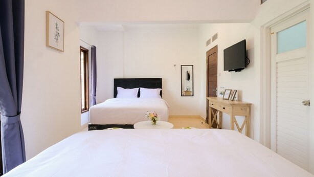 A hotel room with a large bed, a bedside table, a TV mounted on the wall, and a door to the right. - FHStay Maguwo (Depok)
