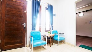 A room with a wooden door, two blue chairs, a small table, and a window with curtains. - FHStay Maguwo (Depok)