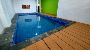 A rectangular indoor swimming pool with blue tiles, surrounded by a wooden deck and white walls. - FHStay Maguwo (Depok)