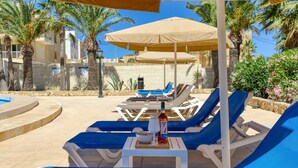 A poolside area with lounge chairs, umbrellas, and a bottle of water. - Ta Frenc Apartments - 2 BDR, 2 BTH (L-Għasri)