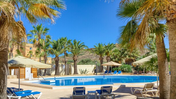 A pool area with lounge chairs and umbrellas, surrounded by palm trees and a clear blue sky. - Ta Frenc Apartments - 2 BDR, 2 BTH (L-Għasri)