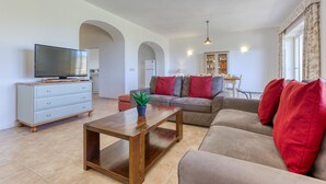 A living room with a sofa, a coffee table, a TV on a cabinet, and a kitchen area in the background. - Ta Frenc Apartments - 2 BDR, 2 BTH (L-Għasri)