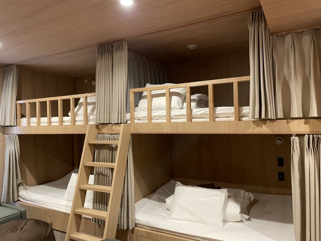 Une chambre avec un lit superposé, une échelle, des rideaux et une petite table.