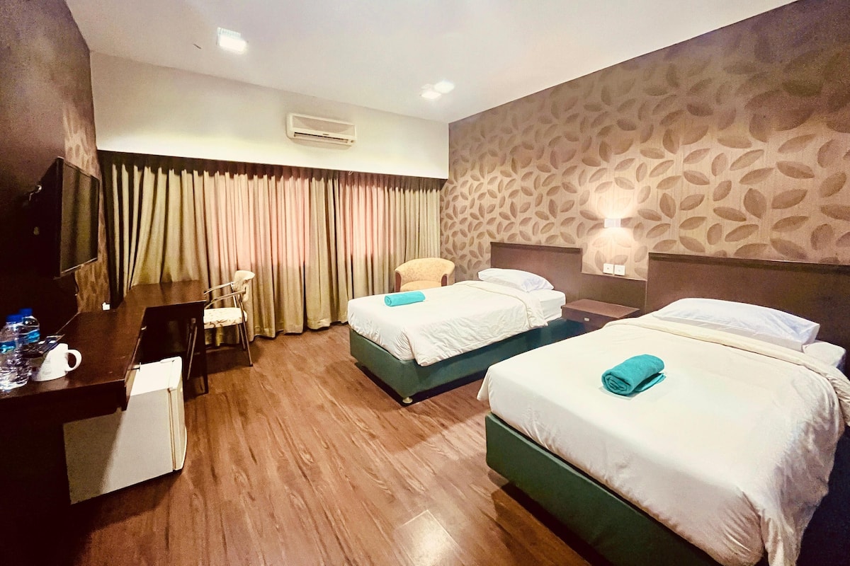 A hotel room with two beds, a desk, a chair, a TV, and a patterned wall.