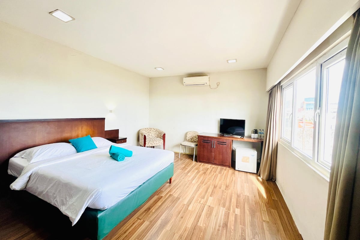 A hotel room with a bed, a desk with a computer, a chair, and a window.