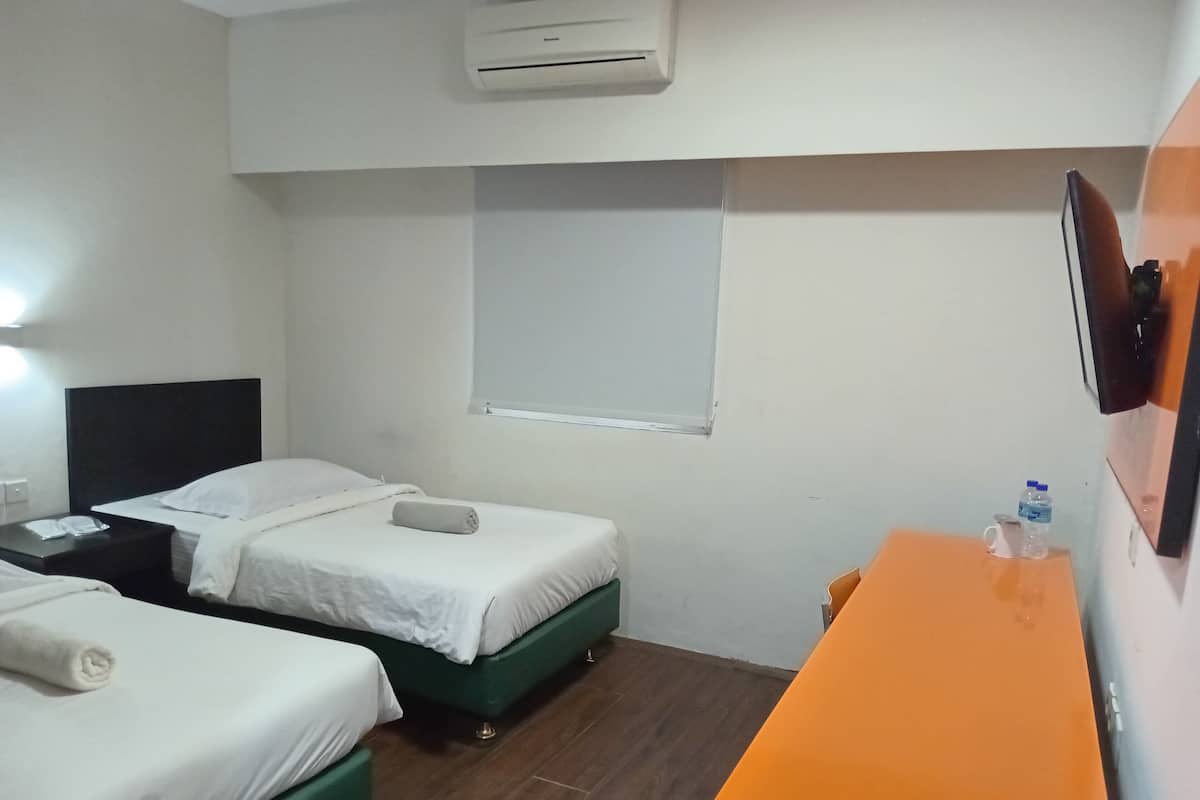 A hotel room with two single beds, a desk, a chair, a TV mounted on the wall, and an air conditioning unit.