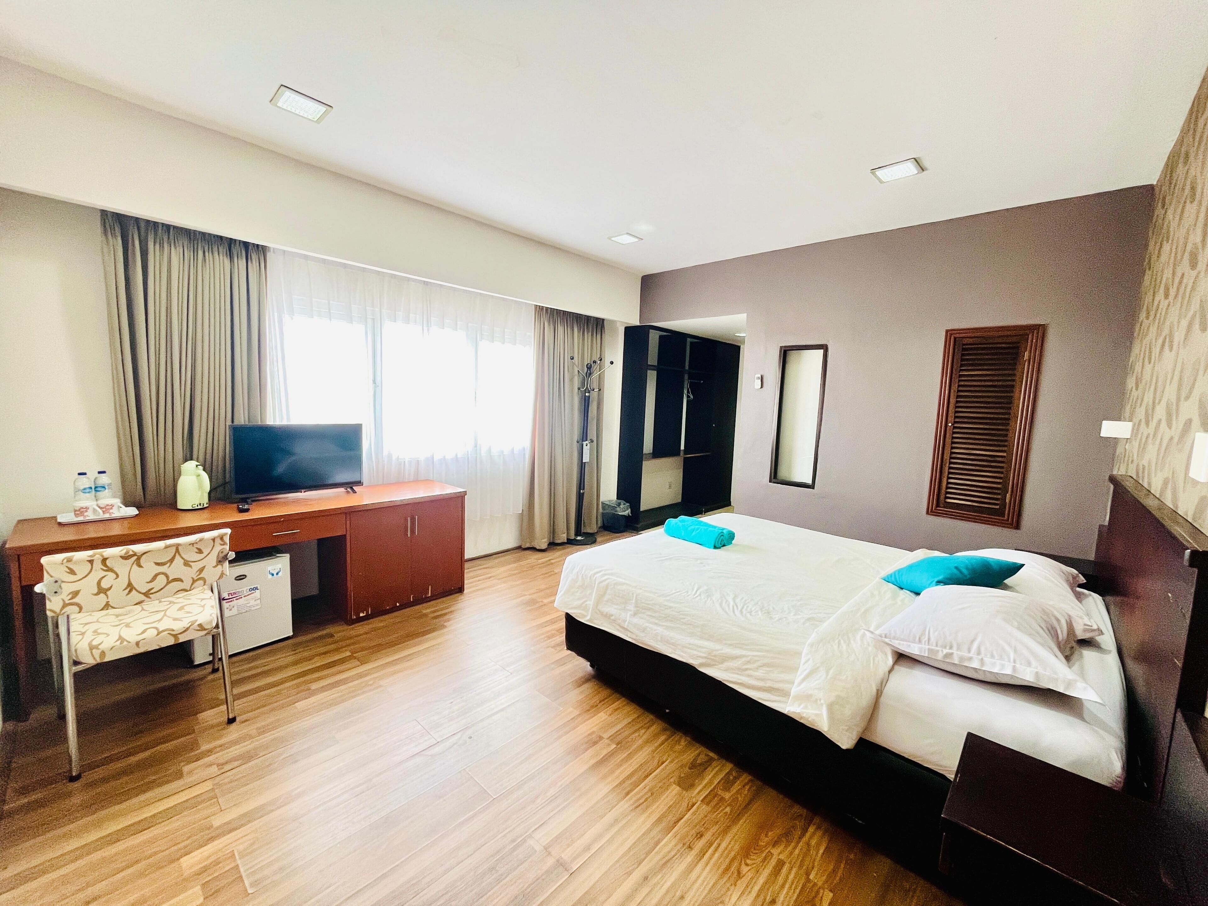 A hotel room with a bed, a desk, a television, a wardrobe, and a shower area.