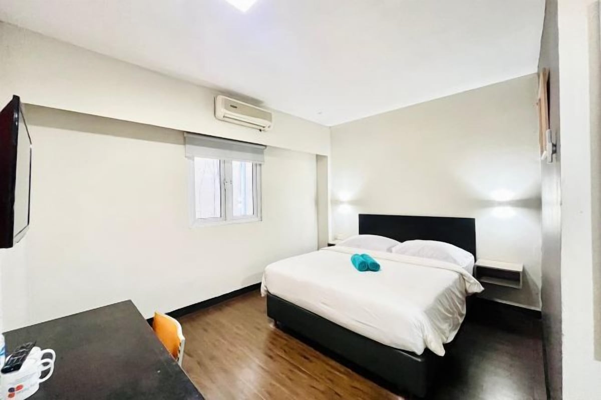 A hotel room with a bed, a desk, an air conditioning unit, and a window.
