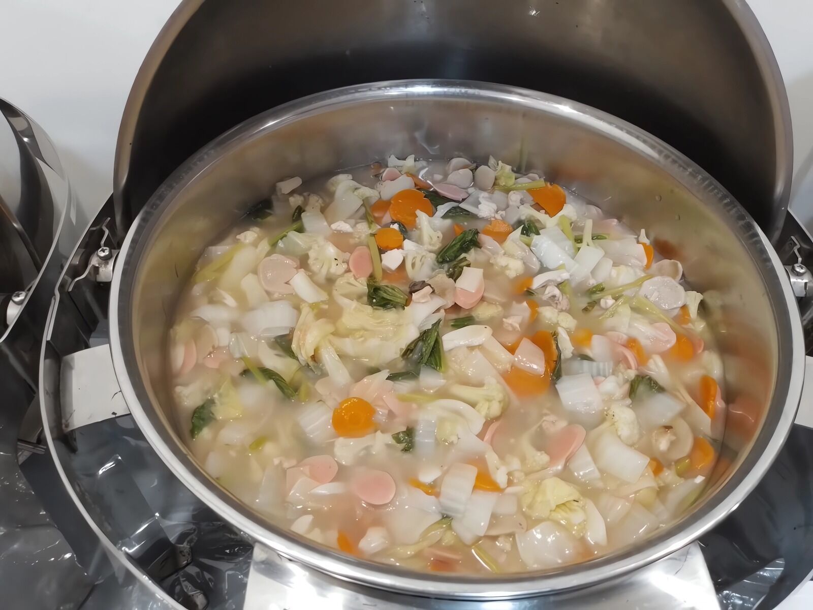 A stainless steel pot on a stove with a variety of vegetables and meat simmering in a broth.