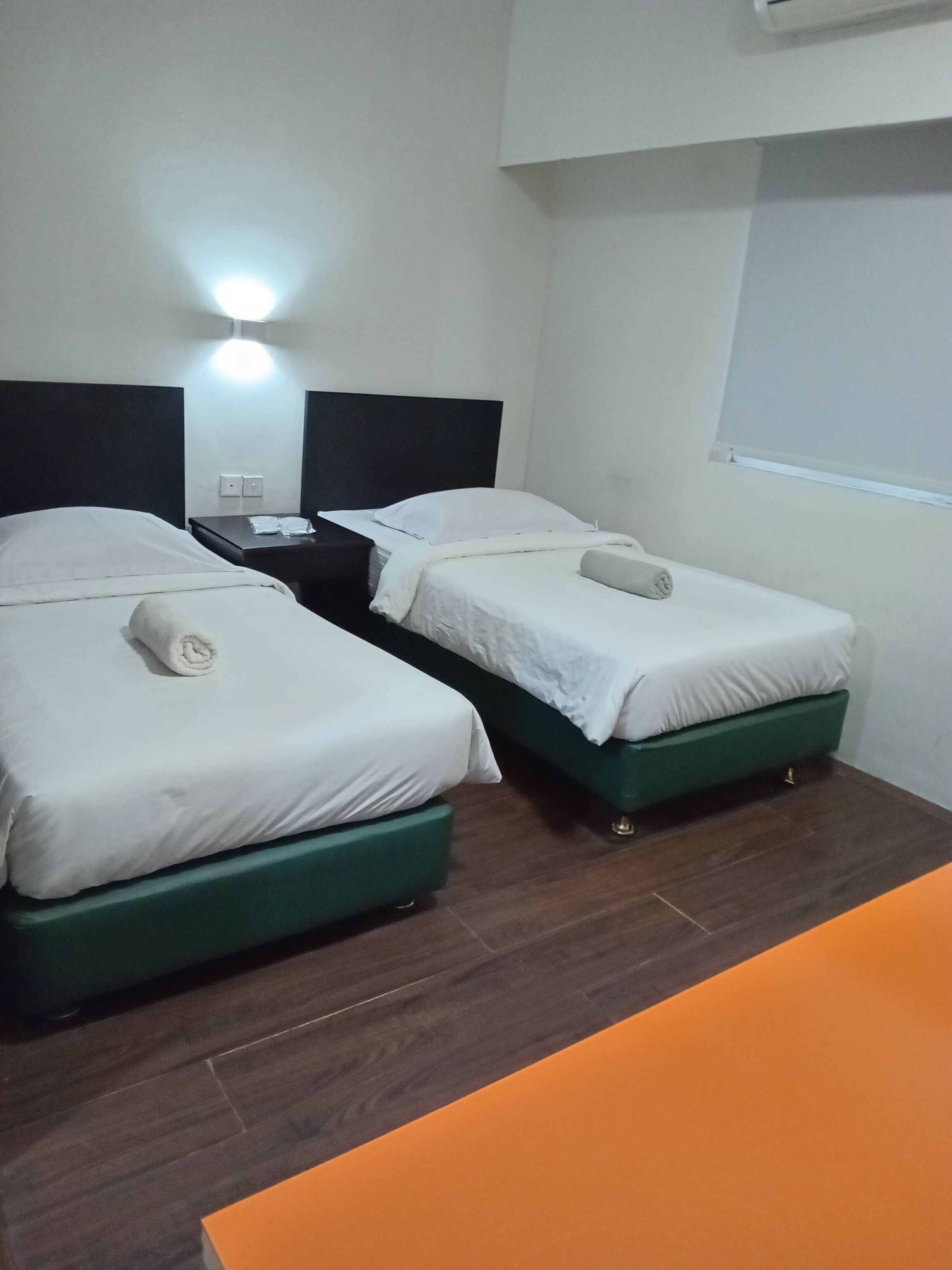 A hotel room with two single beds, a nightstand, a lamp, and a window.