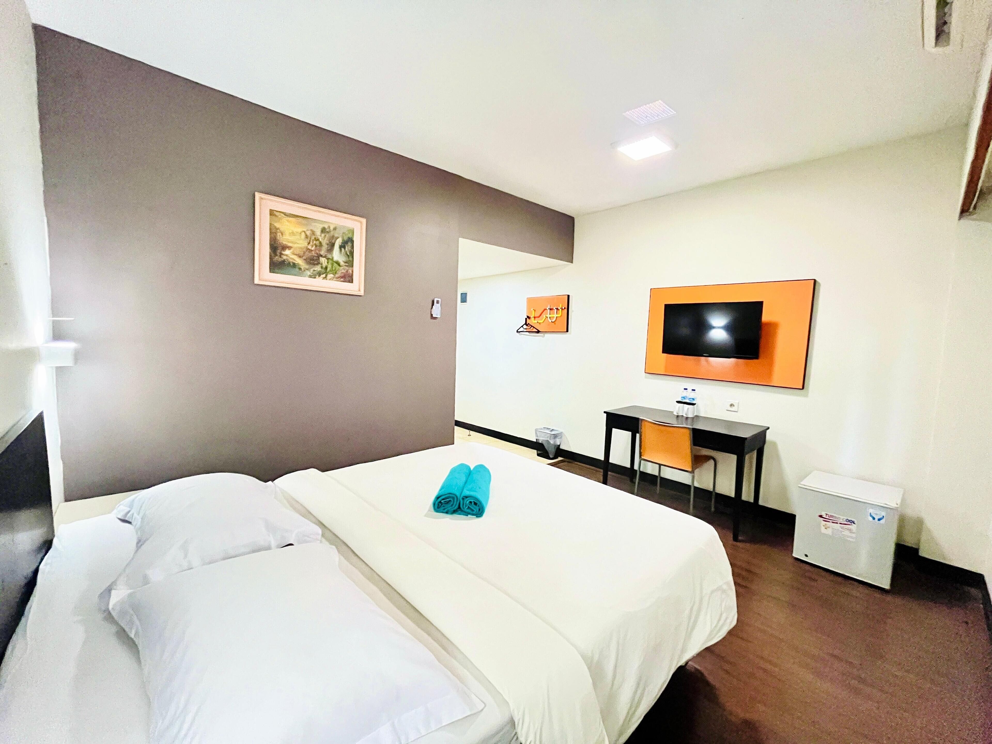 Ett hotellrum med en säng, ett skrivbord, en stol, en tv och en papperskorg.