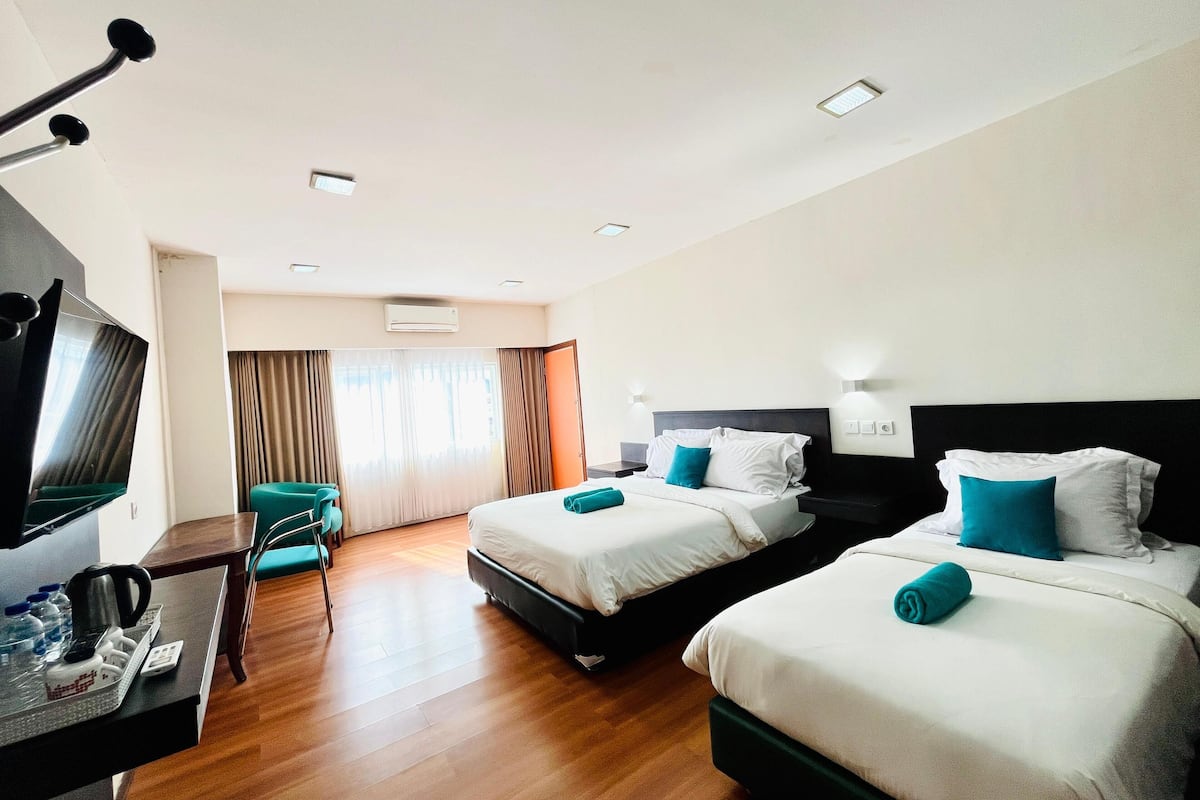 A hotel room with two beds, a desk with a TV, and a seating area with a chair.