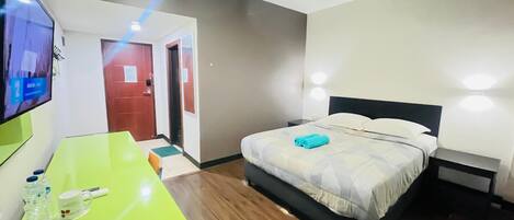 Quarto de hotel com cama, mesa de cabeceira e televisão fixada na parede.