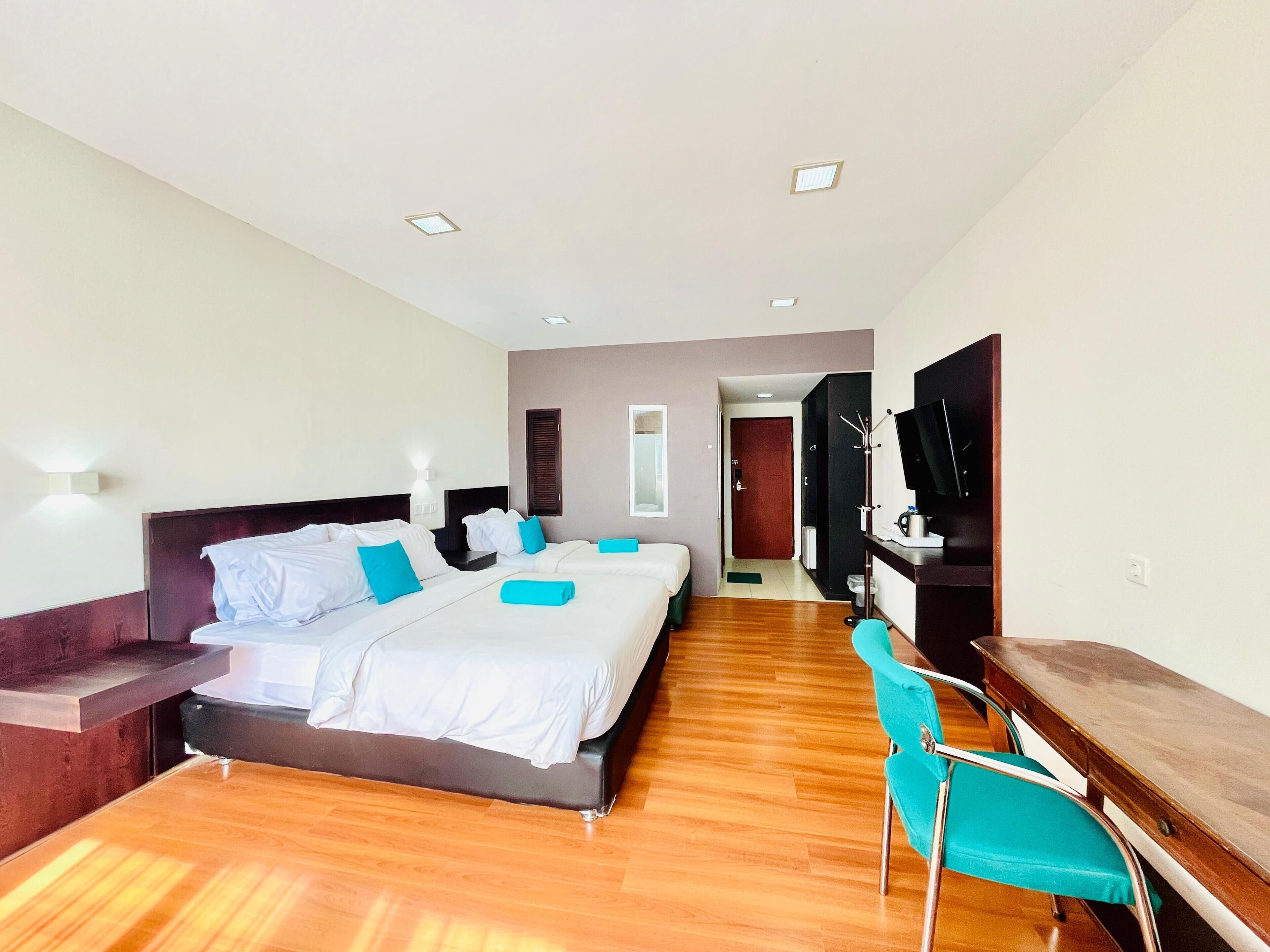 A hotel room with a large bed, a desk, a chair, a TV, and a bathroom visible through an open door.