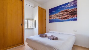 Una camera da letto con un letto, un armadio in legno, una finestra e un dipinto con una vista sulla città.