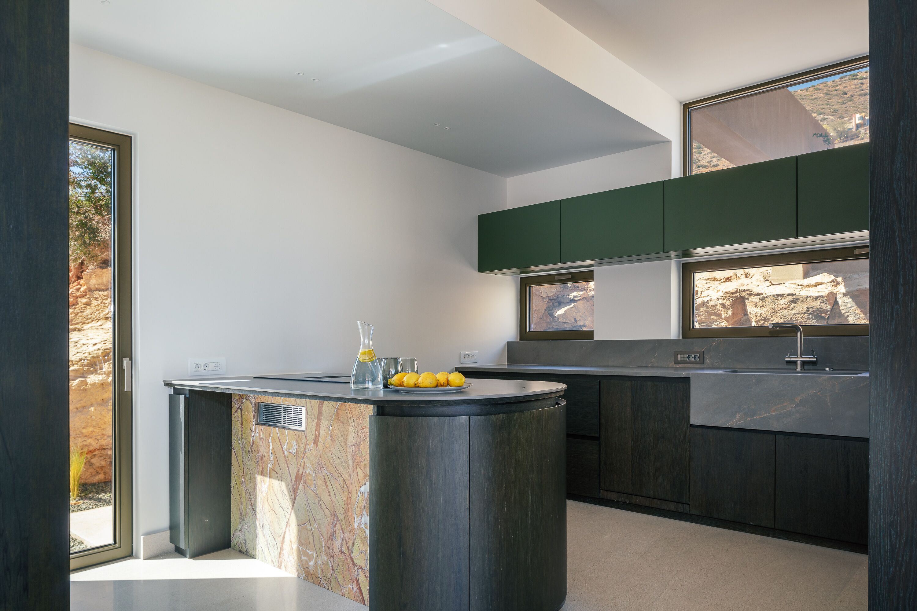 A modern kitchen with a central island, dark cabinetry, and a large window providing a view of the outdoors.