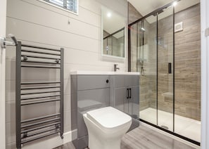 A modern bathroom with a glass shower enclosure, a white toilet, and a grey vanity with cabinets. - 1 bedroom accommodation in Snowdonia (Snowdonia)