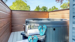 Ein Whirlpool mit Bedienfeld, zwei Weingläser und ein Paar Flip-Flops auf einer Holzterrasse.