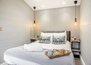 Une chambre d’hôtel moderne avec un grand lit, deux tables de chevet, une petite table et un plateau contenant des articles pour le petit-déjeuner.
