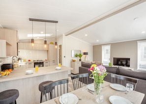 A modern kitchen with a central island, dining area with chairs, a sofa, and a TV in a living room.