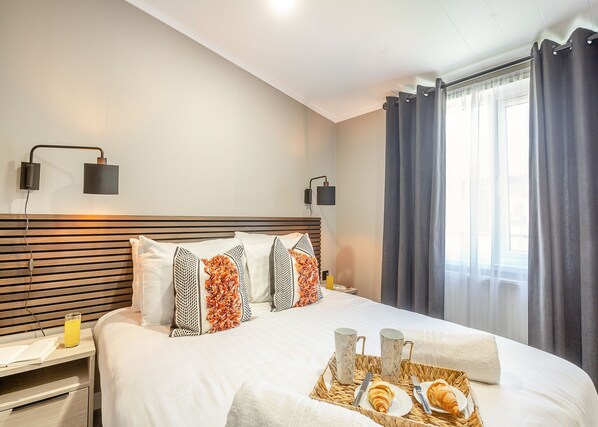 A hotel room with a bed, bedside lamps, a tray with croissants, and a window with curtains.