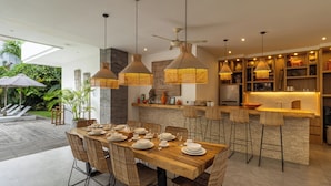 A modern kitchen with a central island, pendant lighting, and a dining area with a wooden table and wicker chairs.