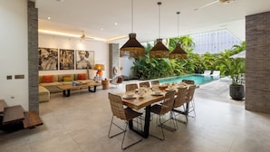 A spacious dining area with a pool view, modern furniture, and a ceiling fan.
