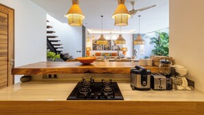 A modern kitchen with a wooden countertop, gas stove, and various appliances. There are hanging pendant lights and a ceiling fan.