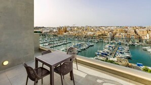 Een balkon met een tafel en stoelen met uitzicht op een jachthaven vol boten en een stadsachtergrond.
