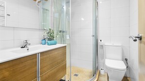 Un baño moderno con cabina de ducha de vidrio, un lavamanos blanco y un inodoro.