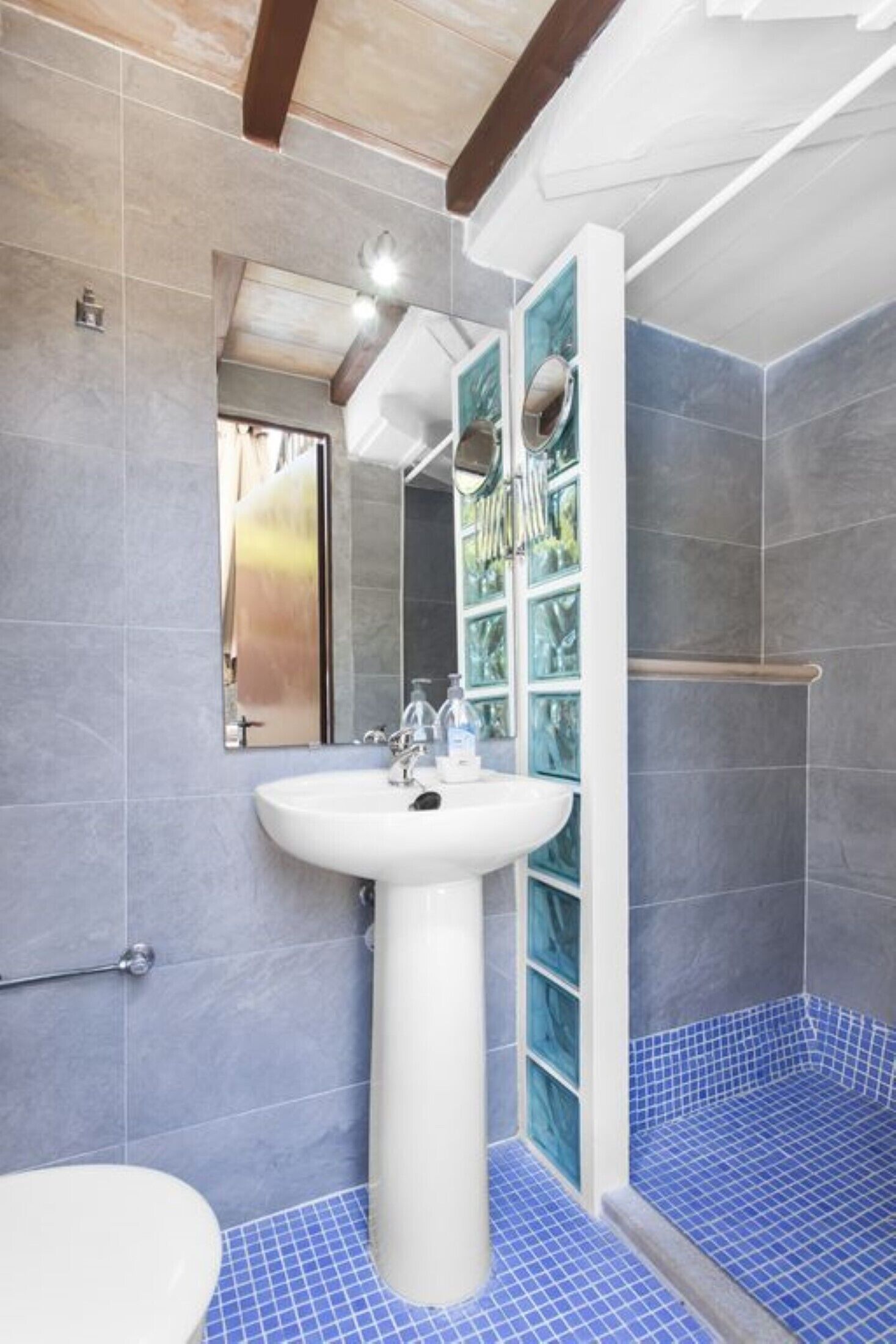 Un bagno con lavabo a piedistallo, uno specchio, box doccia e pavimento piastrellato di blu.