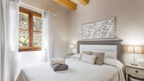 Een net opgemaakt bed met opgerolde handdoeken, een bedlamp en een kunstwerk aan de muur.