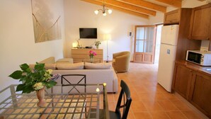 A living room with a sofa, a coffee table, a TV, and a kitchen area with cabinets and a microwave. - Air-Conditioned Holiday Home with Pool, Terrace, Mountain View & Wi-Fi (Sóller)