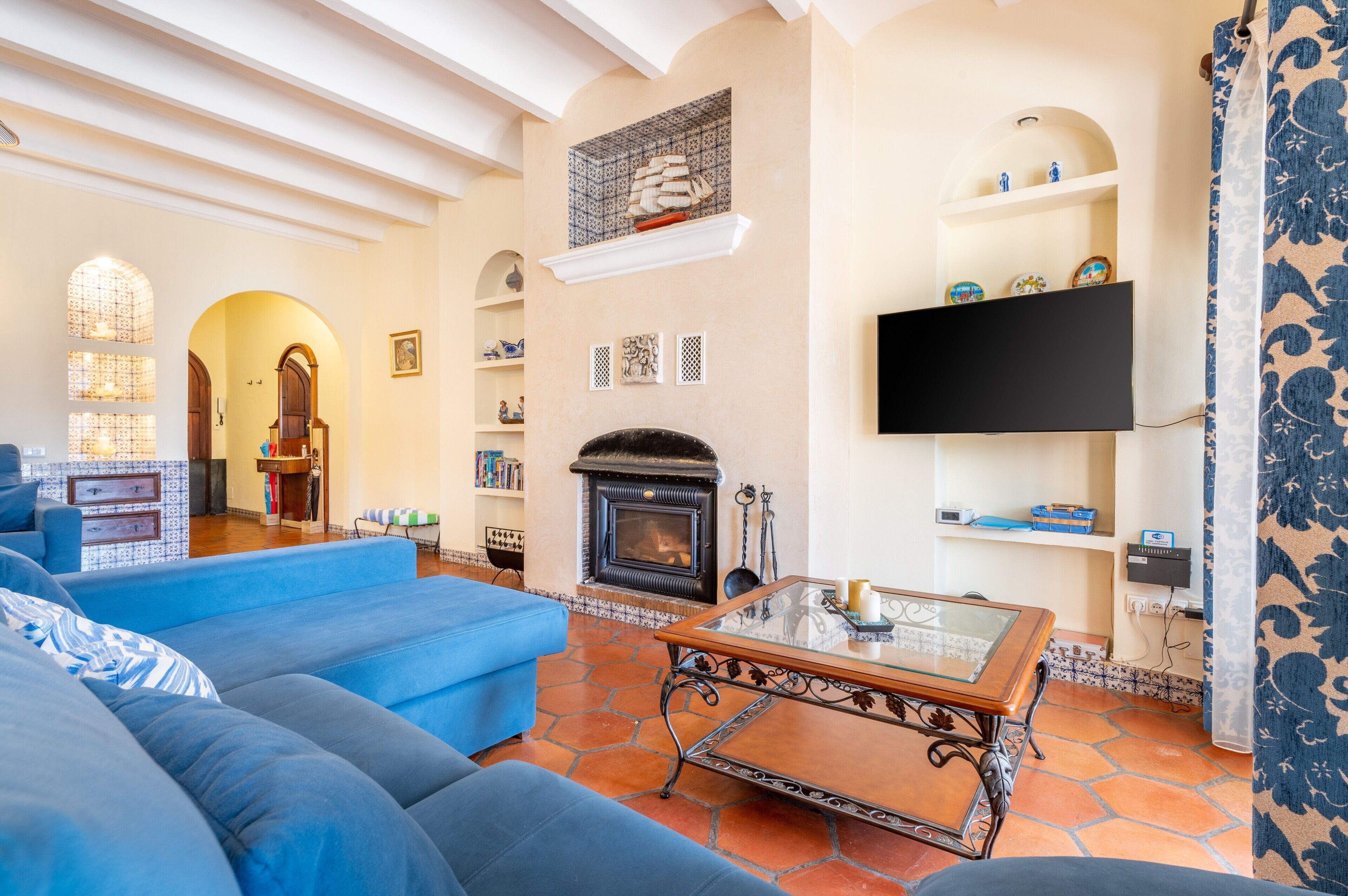 Una sala de estar con chimenea, sofás azules, una mesa de centro de vidrio y un televisor montado en la pared.