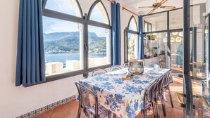 Un comedor con una mesa dispuesta para dos, amplias ventanas en arco y vistas al mar y a las montañas.
