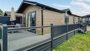 Et moderne træhus med terrasse, udendørs møbler og en overdækket patio.