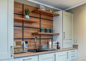 Una cocina moderna con estantes de madera, un fregadero y una cafetera.