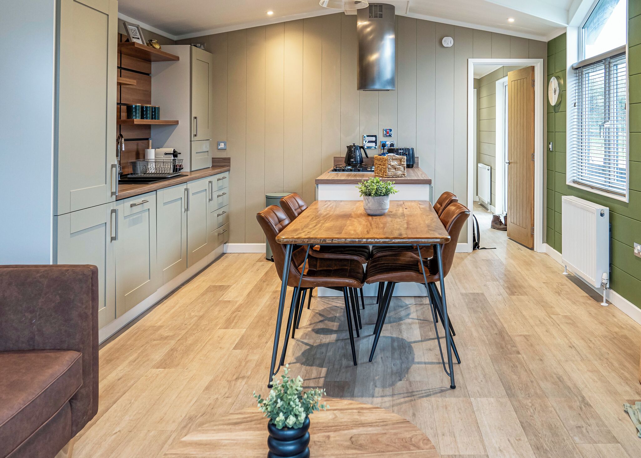 Une cuisine moderne avec un coin repas, un plancher en bois et une grande fenêtre équipée de stores.