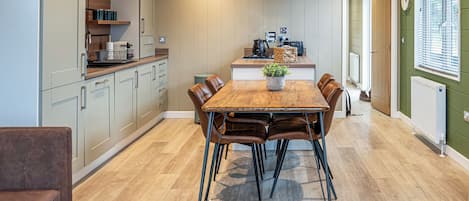 A modern kitchen with a dining area, wooden flooring, and a large window with blinds.