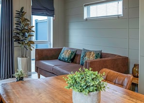 A living room with a brown leather sofa, a wooden dining table, and a potted plant.