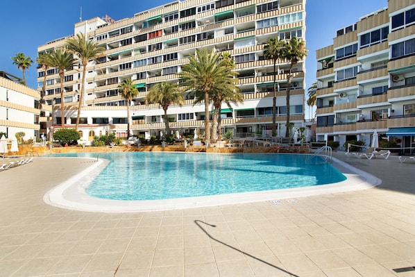 A hotel with a swimming pool, palm trees, and a multi-story building with balconies.