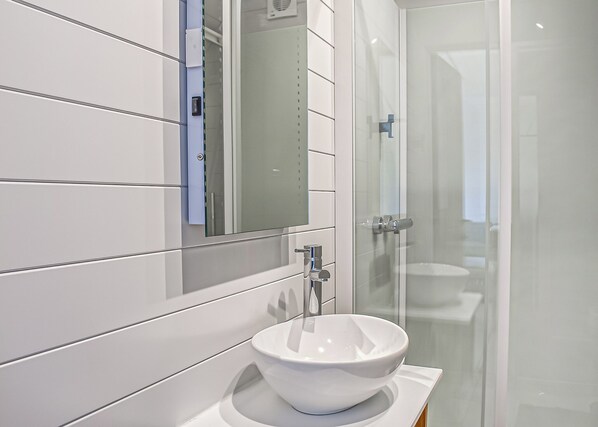 Une salle de bain moderne avec un lavabo blanc, un miroir et une cabine de douche en verre.