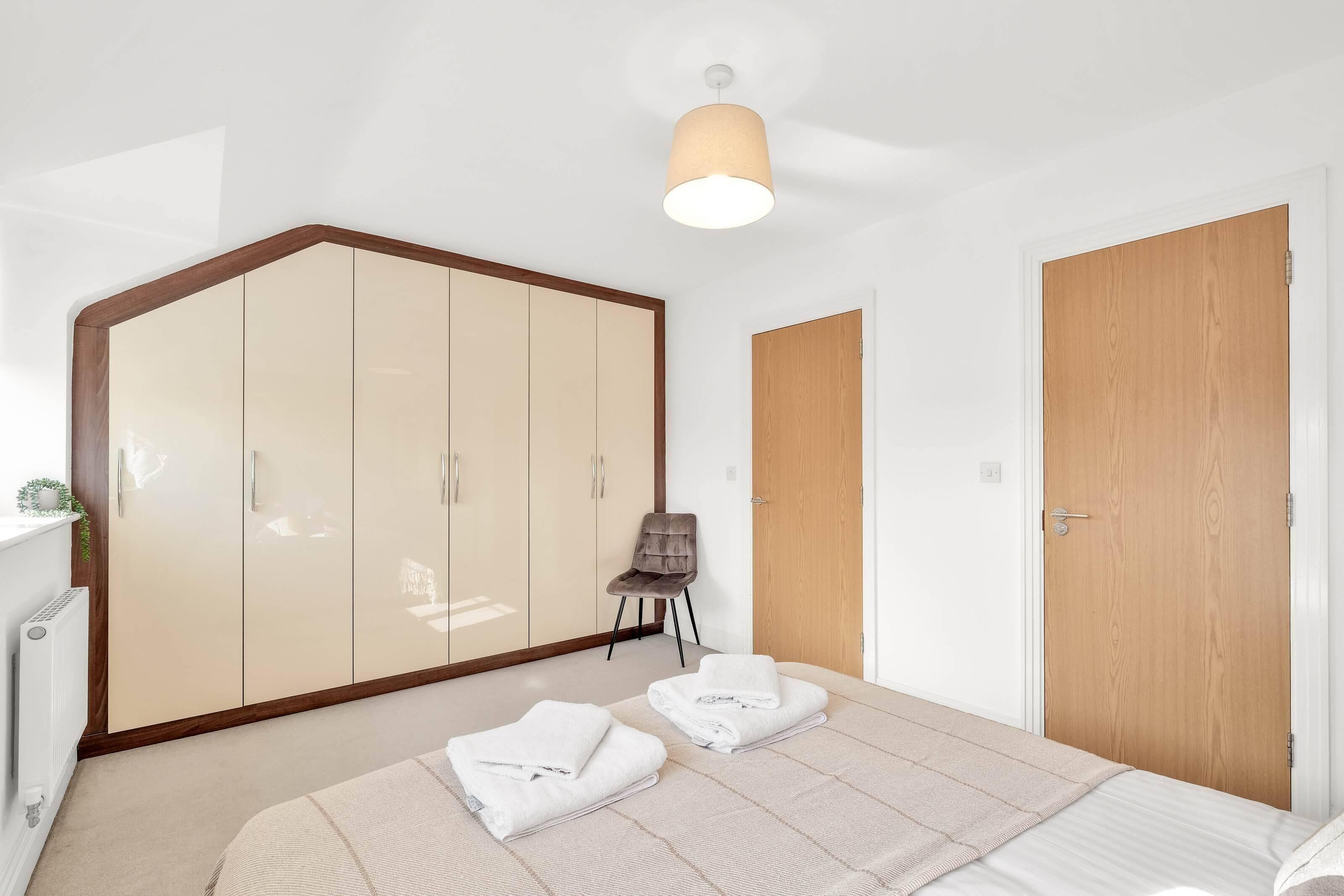 Une chambre avec une grande armoire, une porte en bois, une chaise et deux serviettes pliées posées sur le sol.