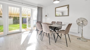 A dining area with a table and chairs, a ceiling fan, a floor lamp, and a sliding glass door leading to a garden. - Foxherne 6 Bdrm, 3BA Hse -17 (Slough)