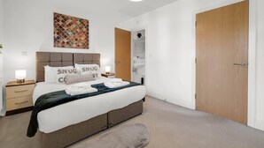 A neatly arranged bedroom with a bed, bedside tables, a hanging light fixture, and a wooden door. - Foxherne 6 Bdrm, 3BA Hse -17 (Slough)