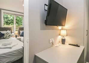 Une chambre d’hôtel avec un lit, un téléviseur fixé au mur, une table de chevet avec une lampe et une fenêtre donnant sur un paysage verdoyant.
